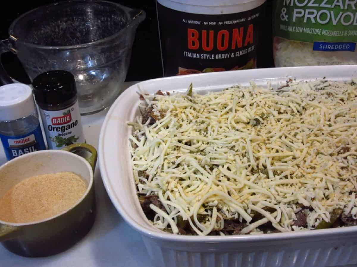 An unbaked cheesy beef bread pudding with ingredients in the background.
