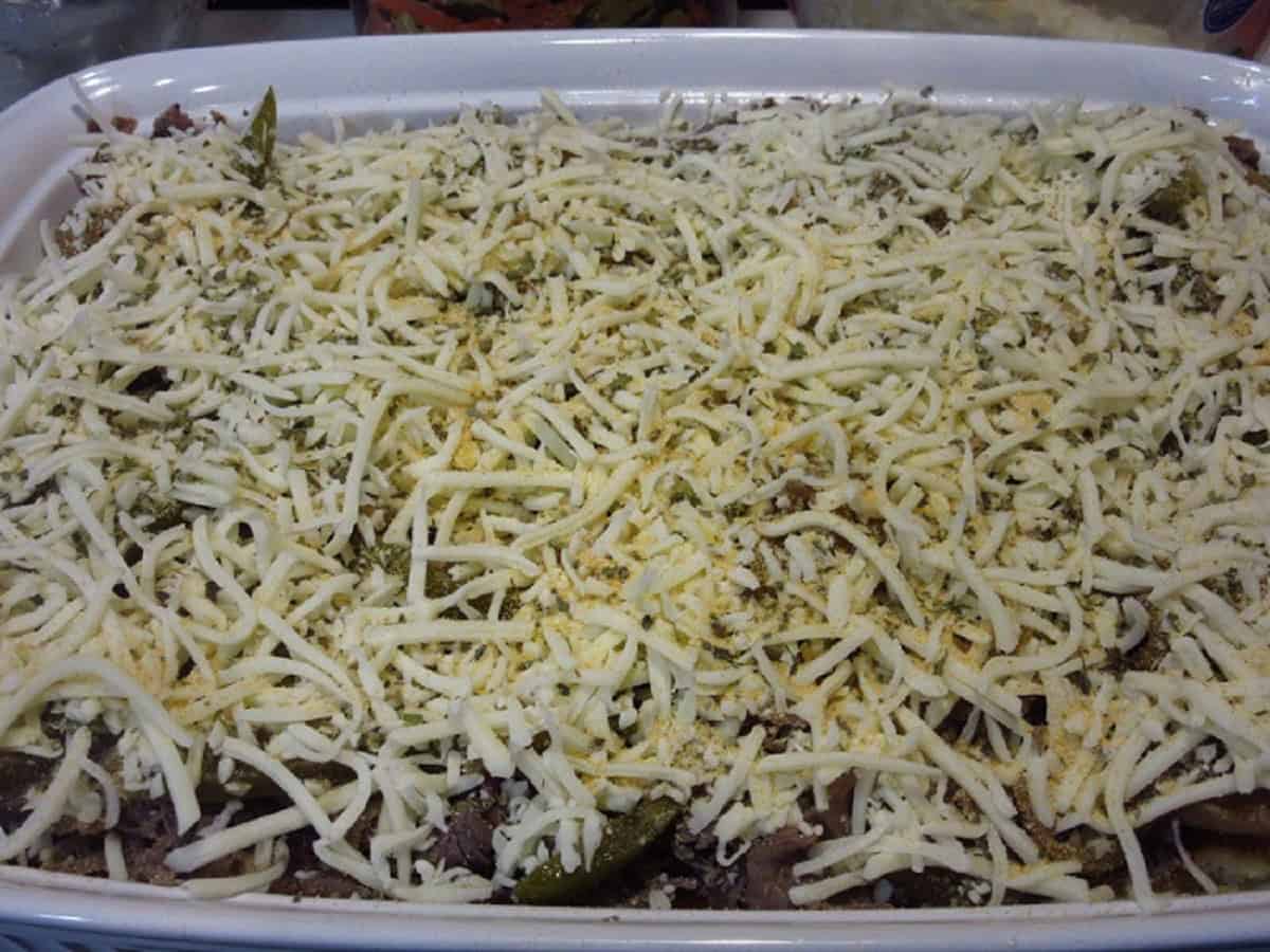 An unbaked Italian Beef Bread Pudding in a casserole dish with shredded cheese on top.