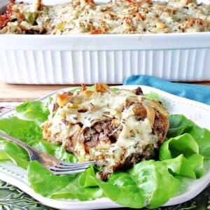 A serving of Italian Beef Bread Pudding on a white plate with lettuce and a fork.