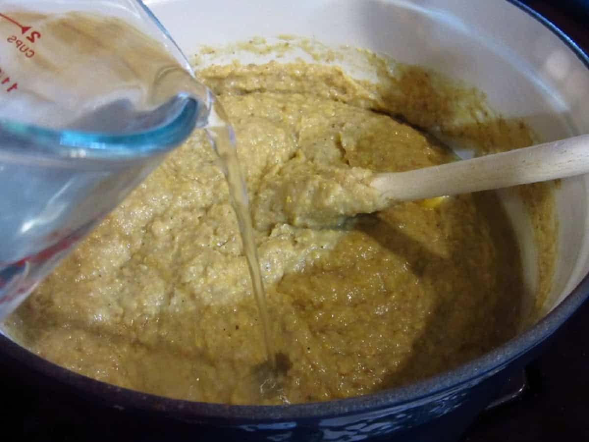 Water being added to a pot of thick corn chowder.