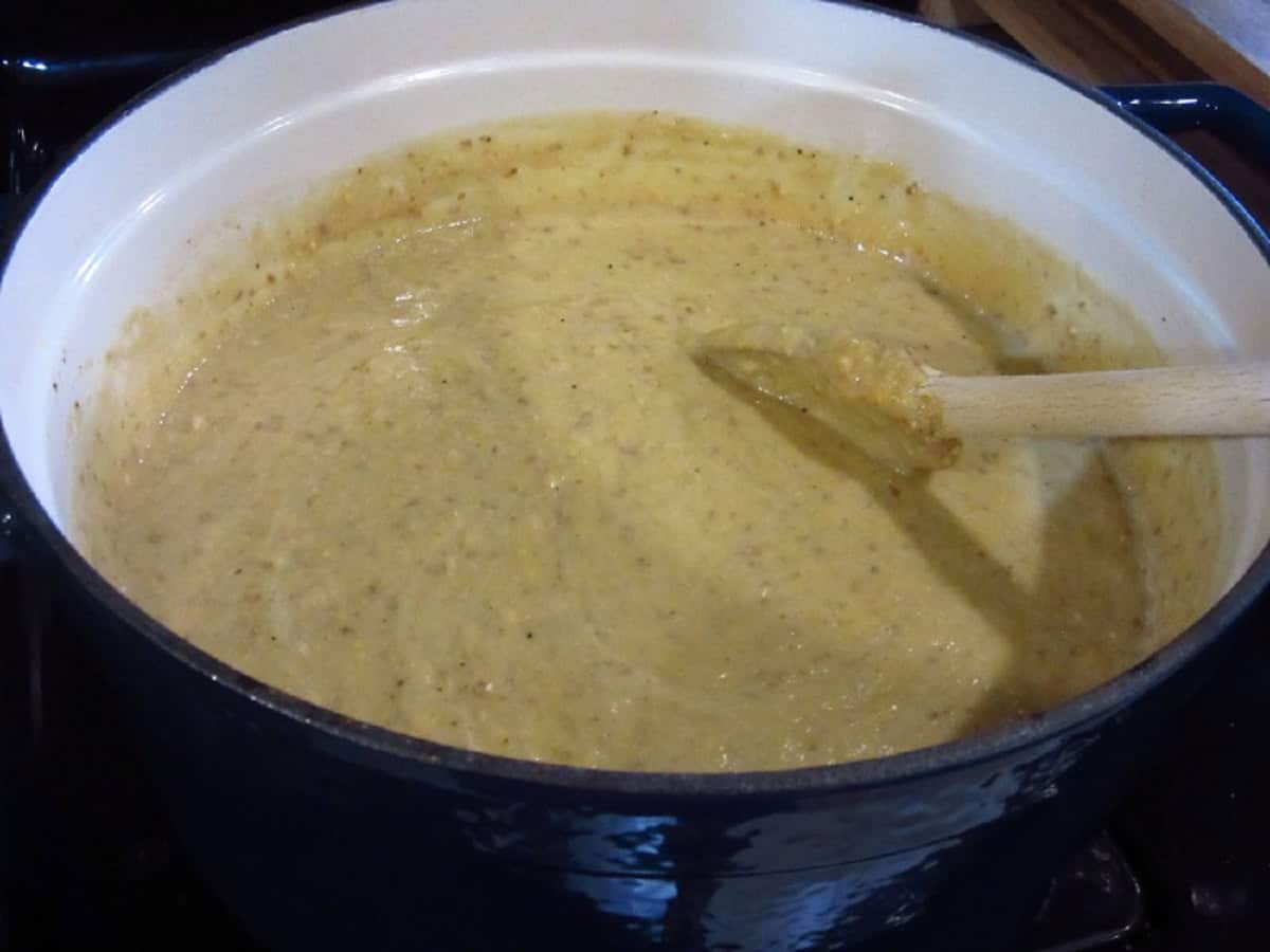 A wooden spoon in a Dutch oven filled with roasted corn and potato chowder.
