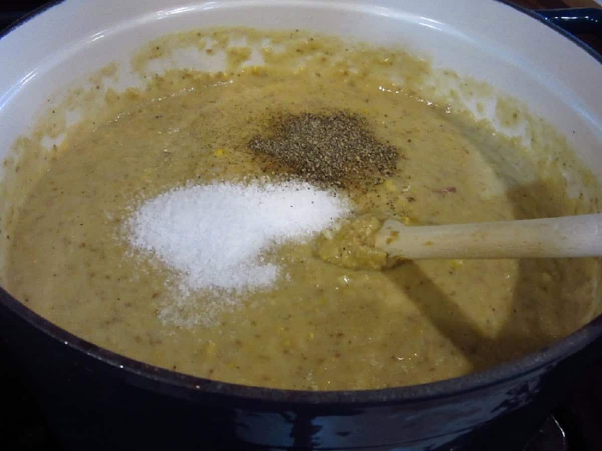 Salt and pepper added to a pot of corn chowder.