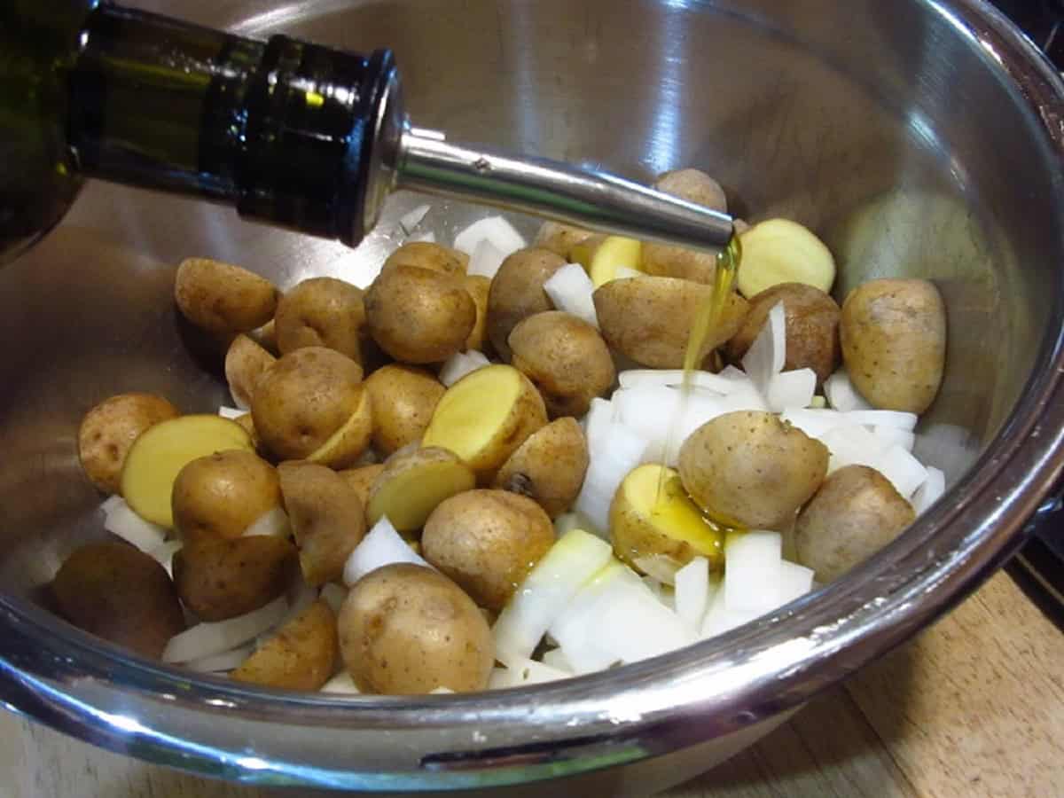 Adding oil to a bowl of chopped onions and potatoes.