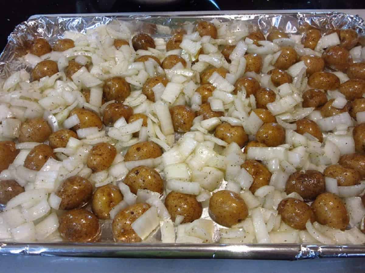 Oiled potatoes and onions on a baking sheet ready for the oven.
