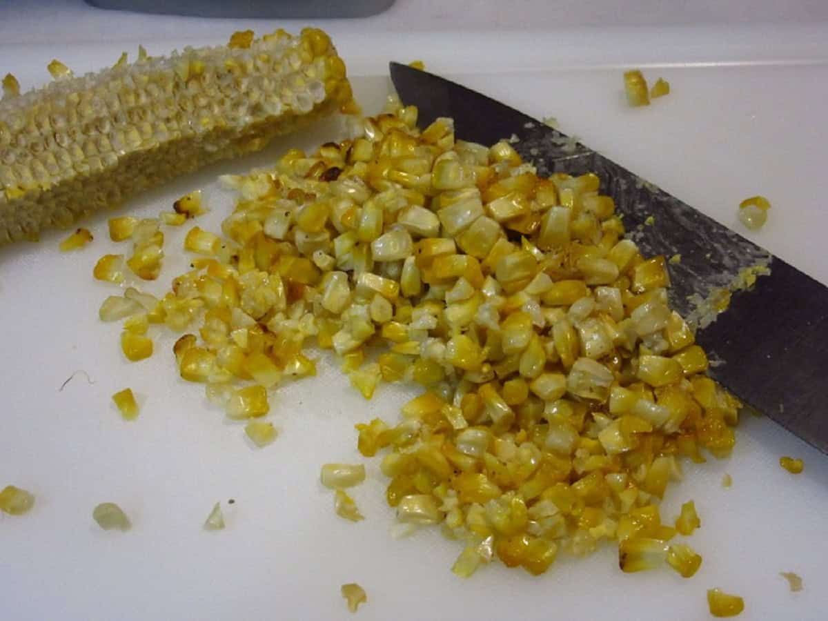 Roasted corn kernels cut off the cob on a cutting board.
