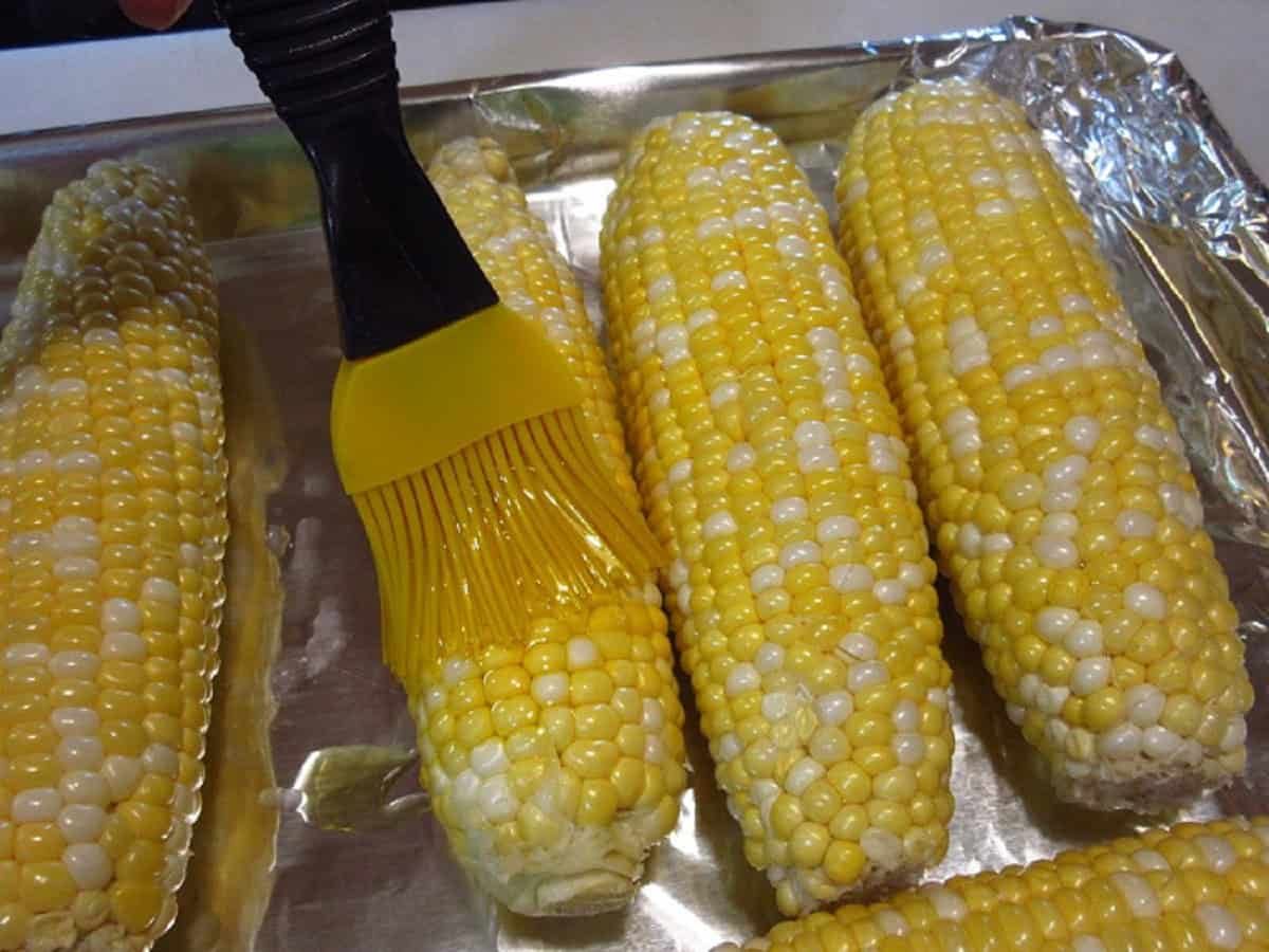 A pastry brush adding oil to corn on the cob.