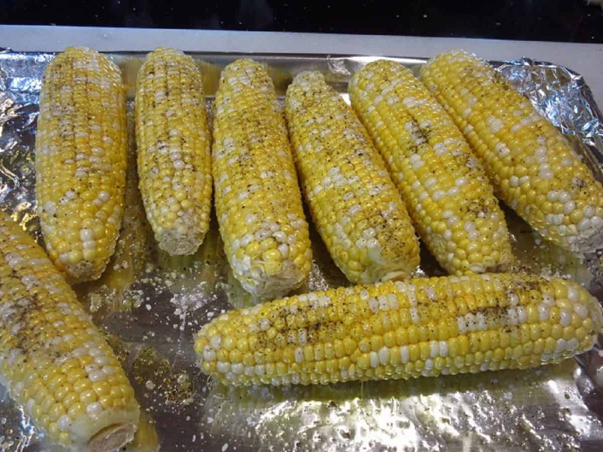Corn on the cob on a baking sheet seasoned with salt and pepper.