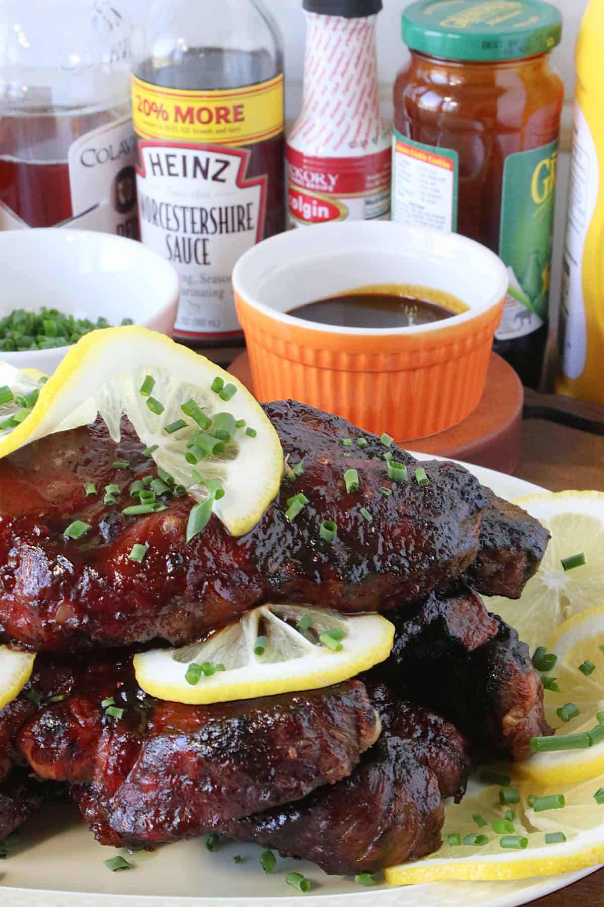 A platter of BBQ country ribs in the forefront with bottles of different ingredients in the background.
