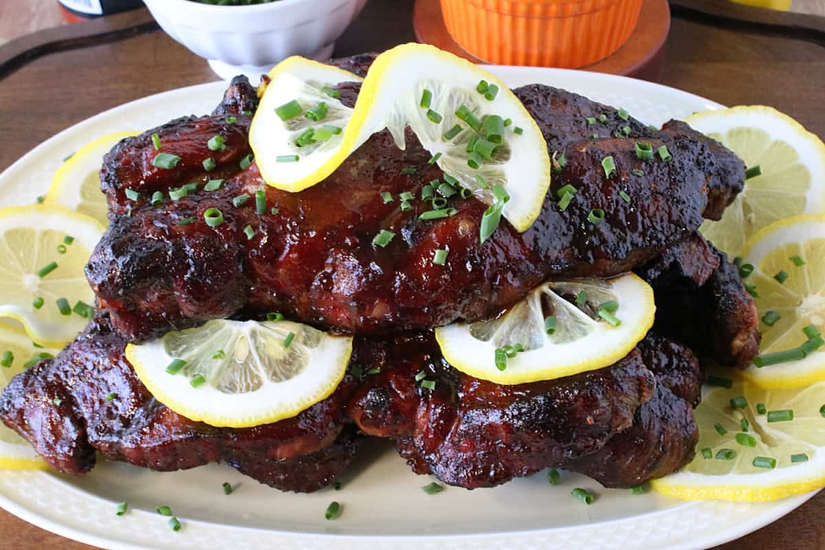 A platter filled with Spicy BBQ Country Ribs with lemon slices and chives on top.