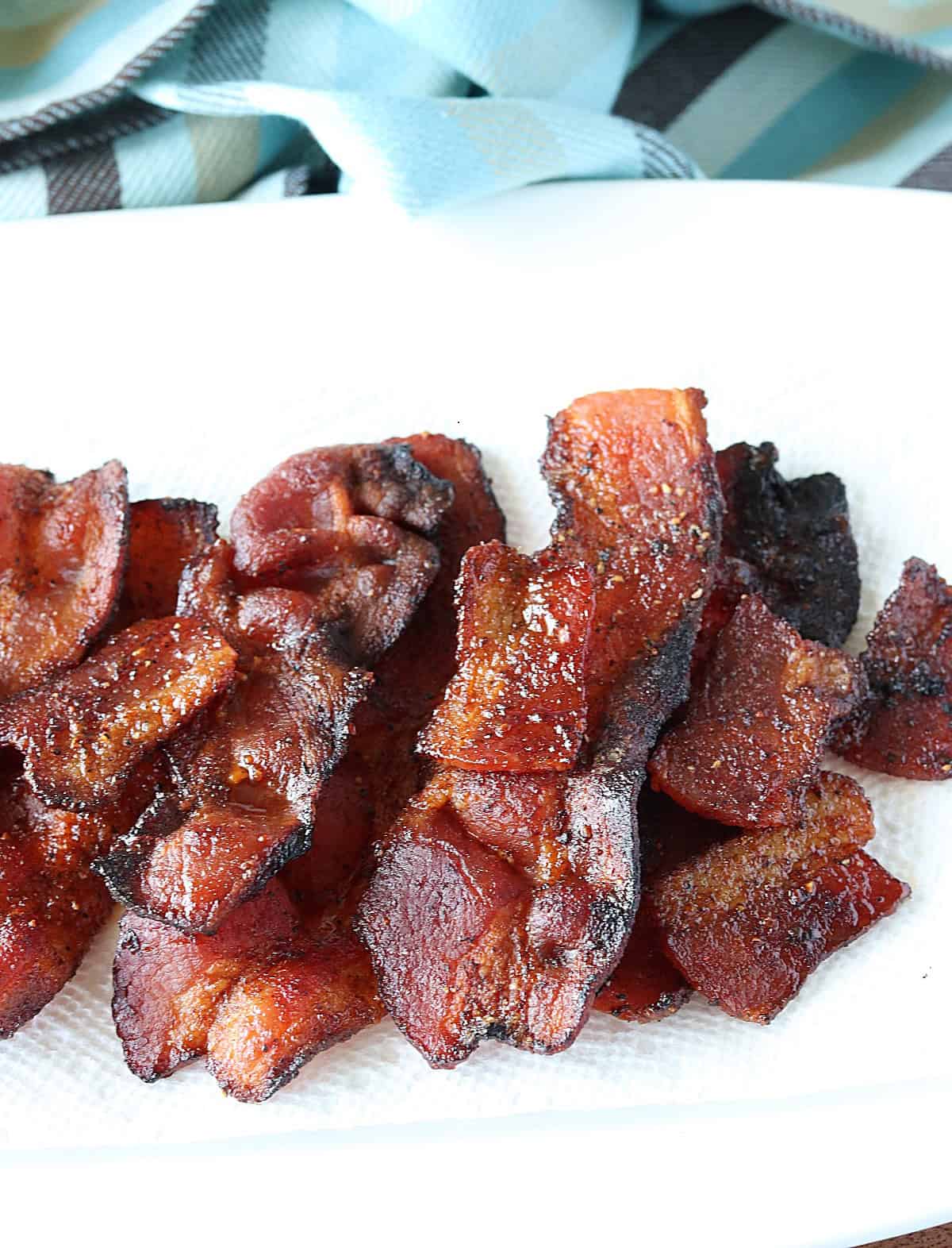 A blue stripped napkin in back of a white platter filled with Air Fryer Brown Sugar Bacon.