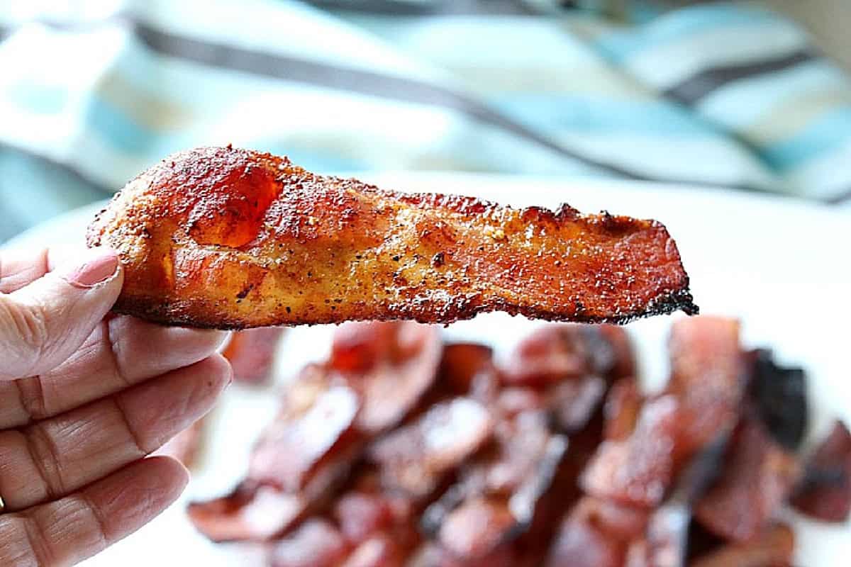 A hand holding a crisp slice of air fryer bacon.