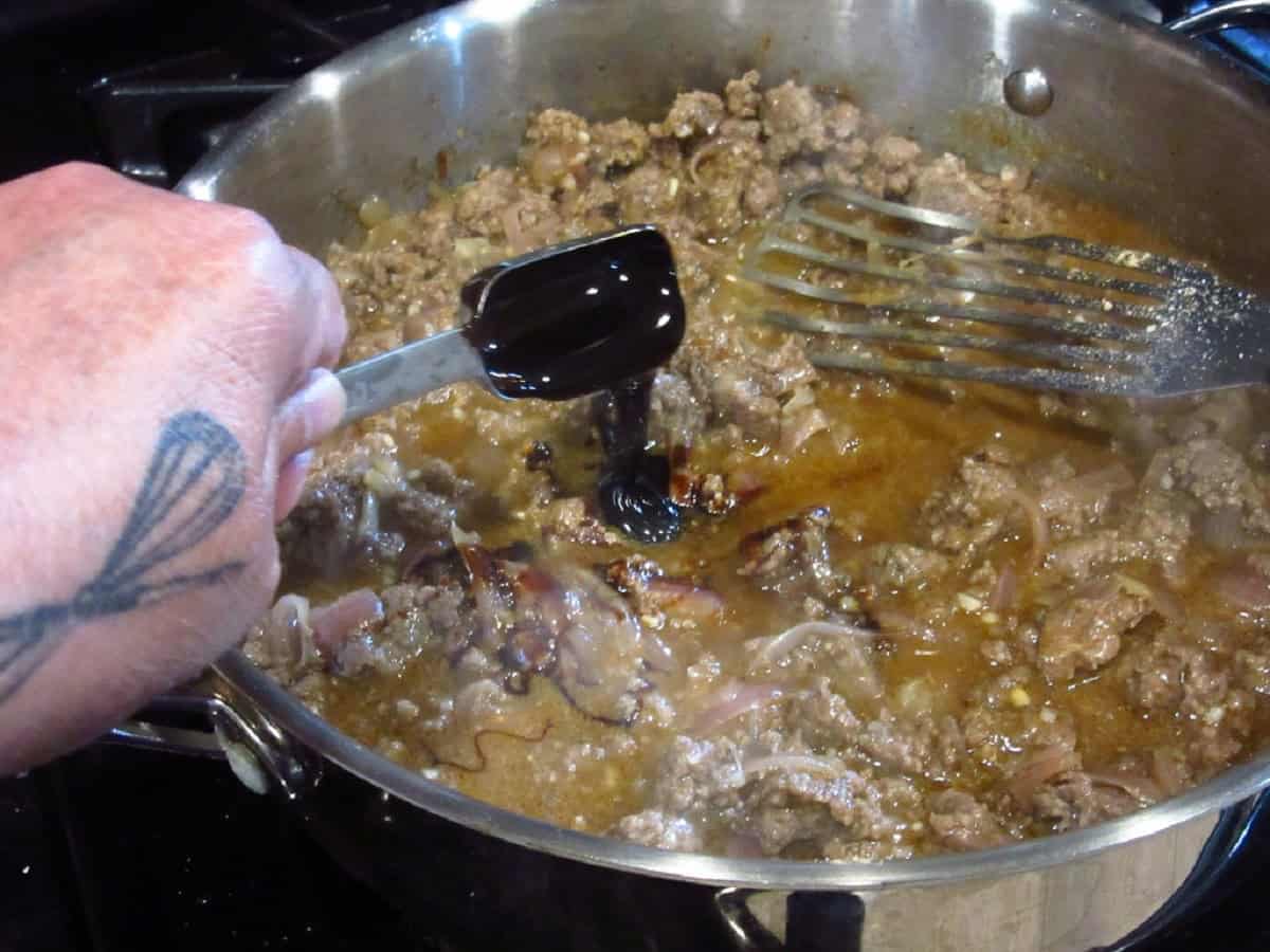 A small amount of molasses being added into a skillet of ground beef sauerbraten.