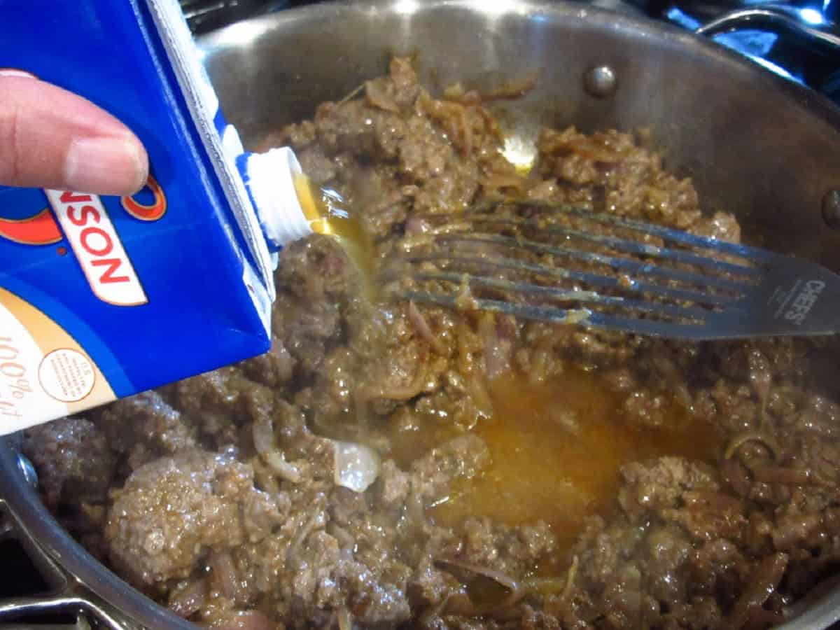 Beef broth being added to a skillet with ground beef.