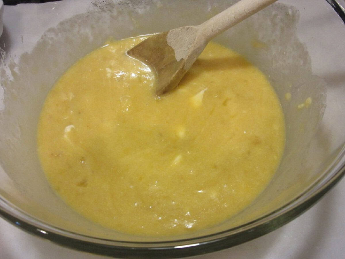 A glass bowl with a thin banana bread mixture and a wooden spoon.