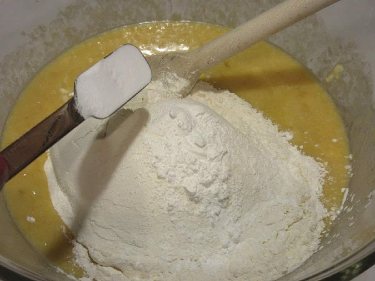 Flour and baking soda being added to a banana bread batter in a glass bowl.