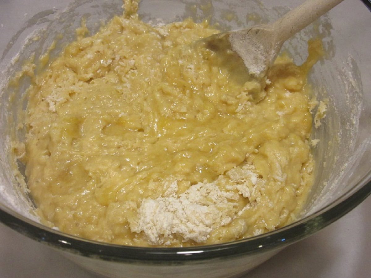 A banana bread batter in a glass bowl with a wooden spoon.