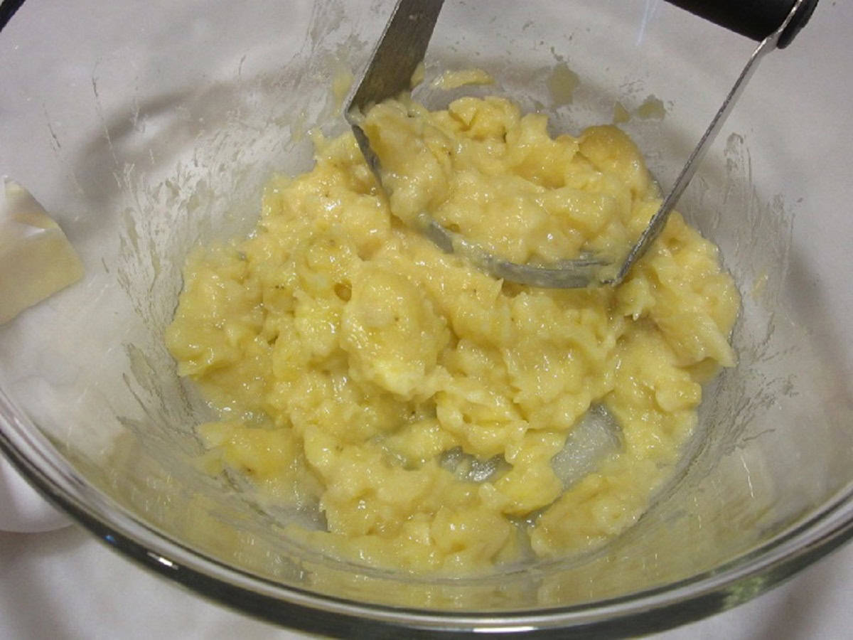 Mashed bananas in a glass bowl with a pastry blender.