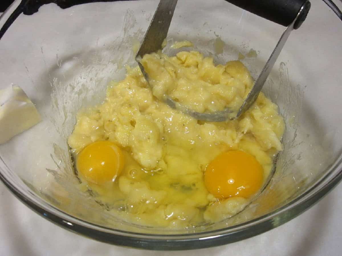 Two eggs and a mashed banana mixture in a bowl with a pastry blender.