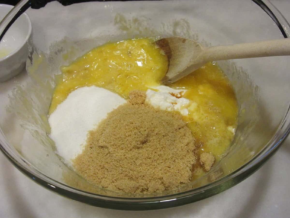 A mashed up banana bread mixture with sugar and brown sugar in the bowl.
