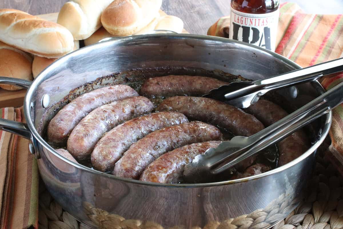 Cooked bratwurst in a skillet with tongs.