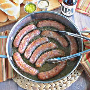 A skillet full of beer braised bratwurst with a pair of tongs on a cooling pad.