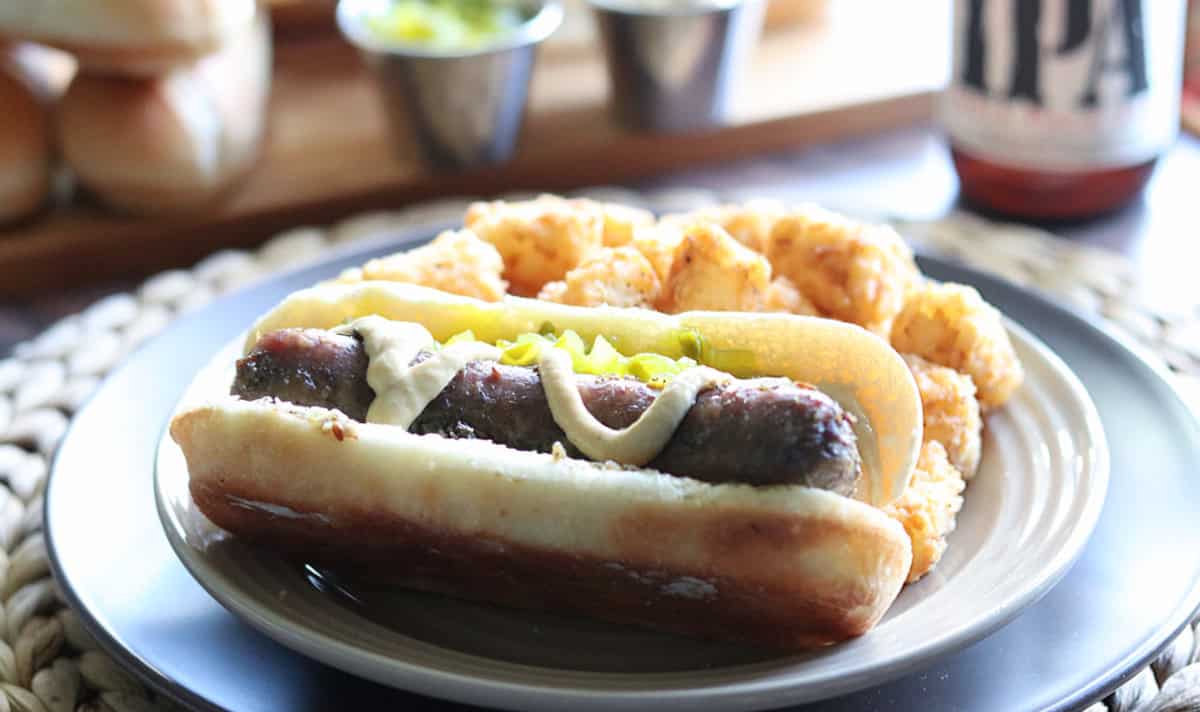 A beer-braised bratwurst on a plate with tater tots.