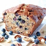 A look inside a Blueberry Banana Bread with white chocolate chips, blueberries, and pecans on the table.