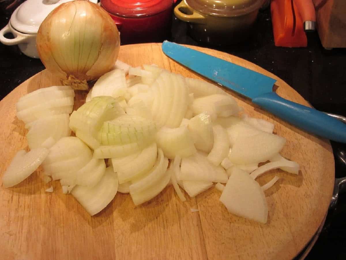 Sliced onions on a cutting board along with a blue knife.