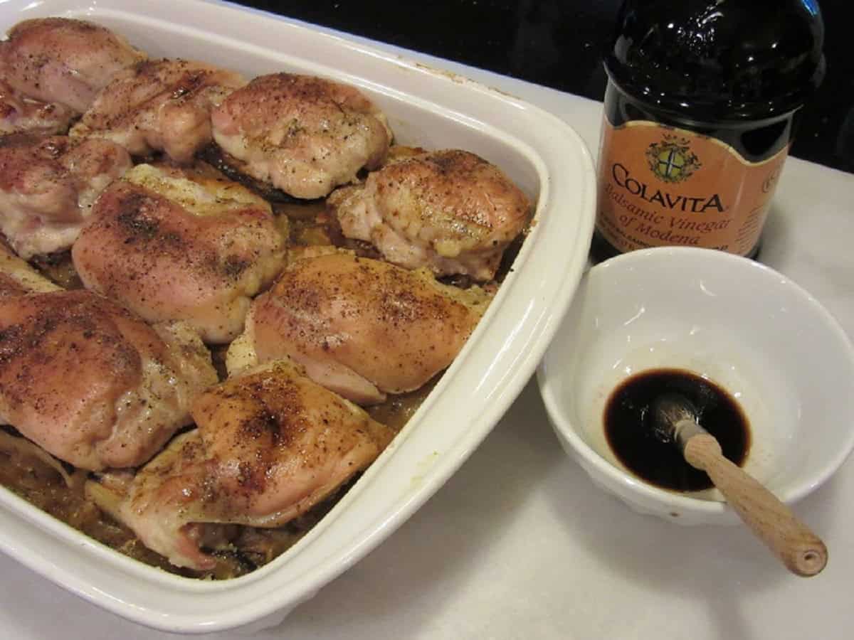 Balsamic vinegar in a small bowl next to a casserole dish with chicken thighs.