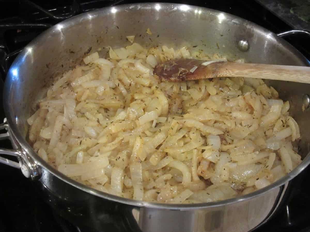 Sliced onions in large skillet with a wooden spoon.
