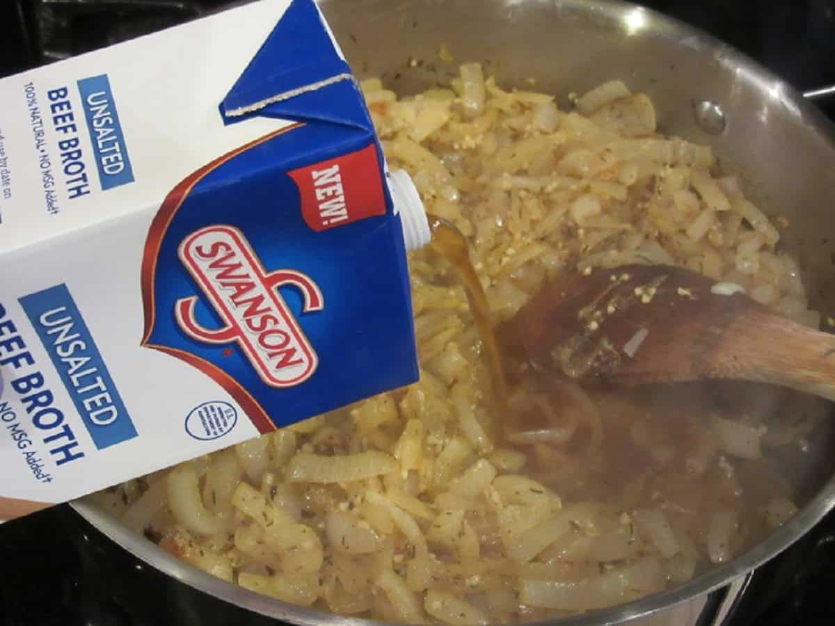 Beef broth being added to a skillet with caramelized onions.