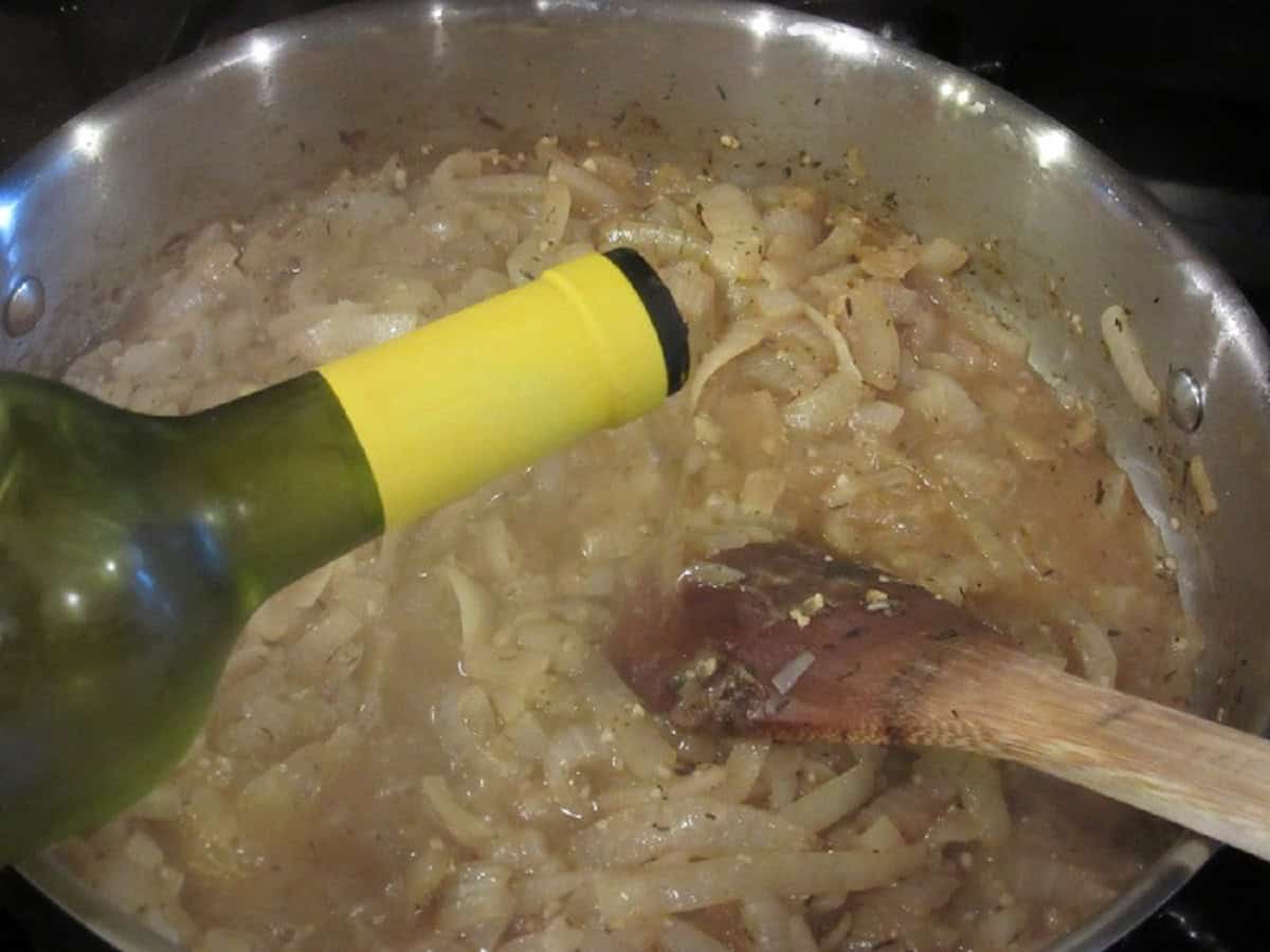 White wine being added to a large skillet of caramelized onions.