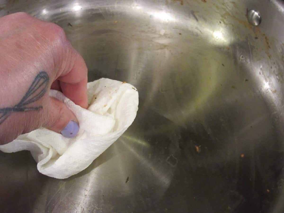 A hand wiping out a skillet with a paper towel.