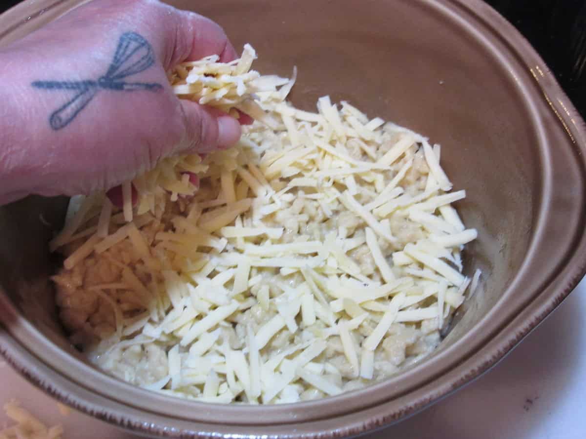 A hand adding shredded cheese on top of German dumplings.