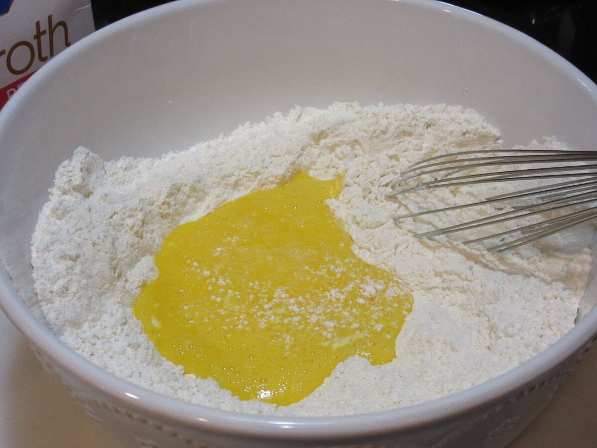 Beaten egg and flour in a white bowl with a whisk.
