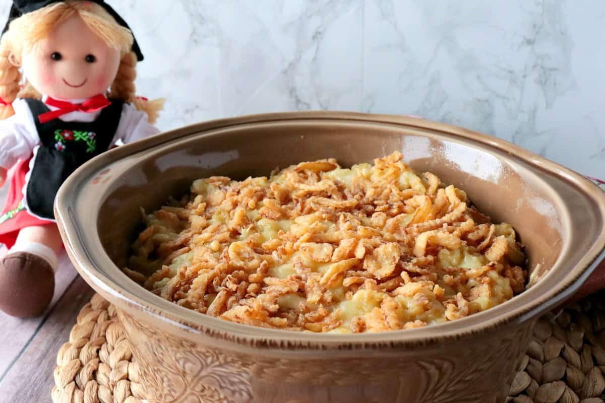 A German doll behind a casserole dish of Layered German Spaetzle Casserole.