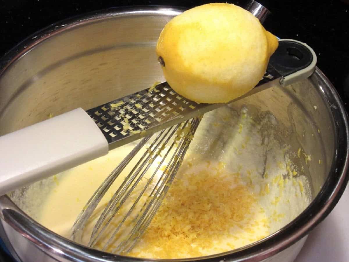A fresh lemon being zested into a bowl of cake batter.