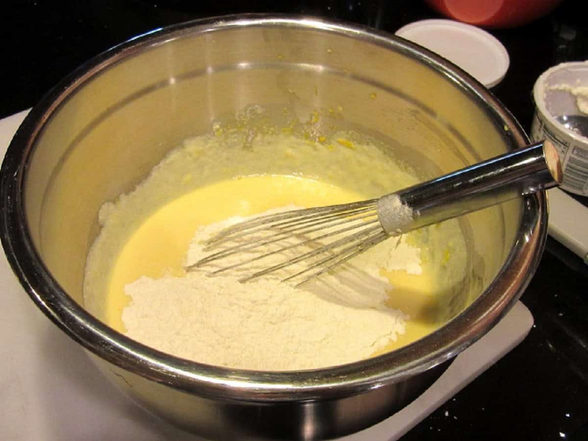 A whisk in a large bowl with flour and a lemon ricotta mixture.