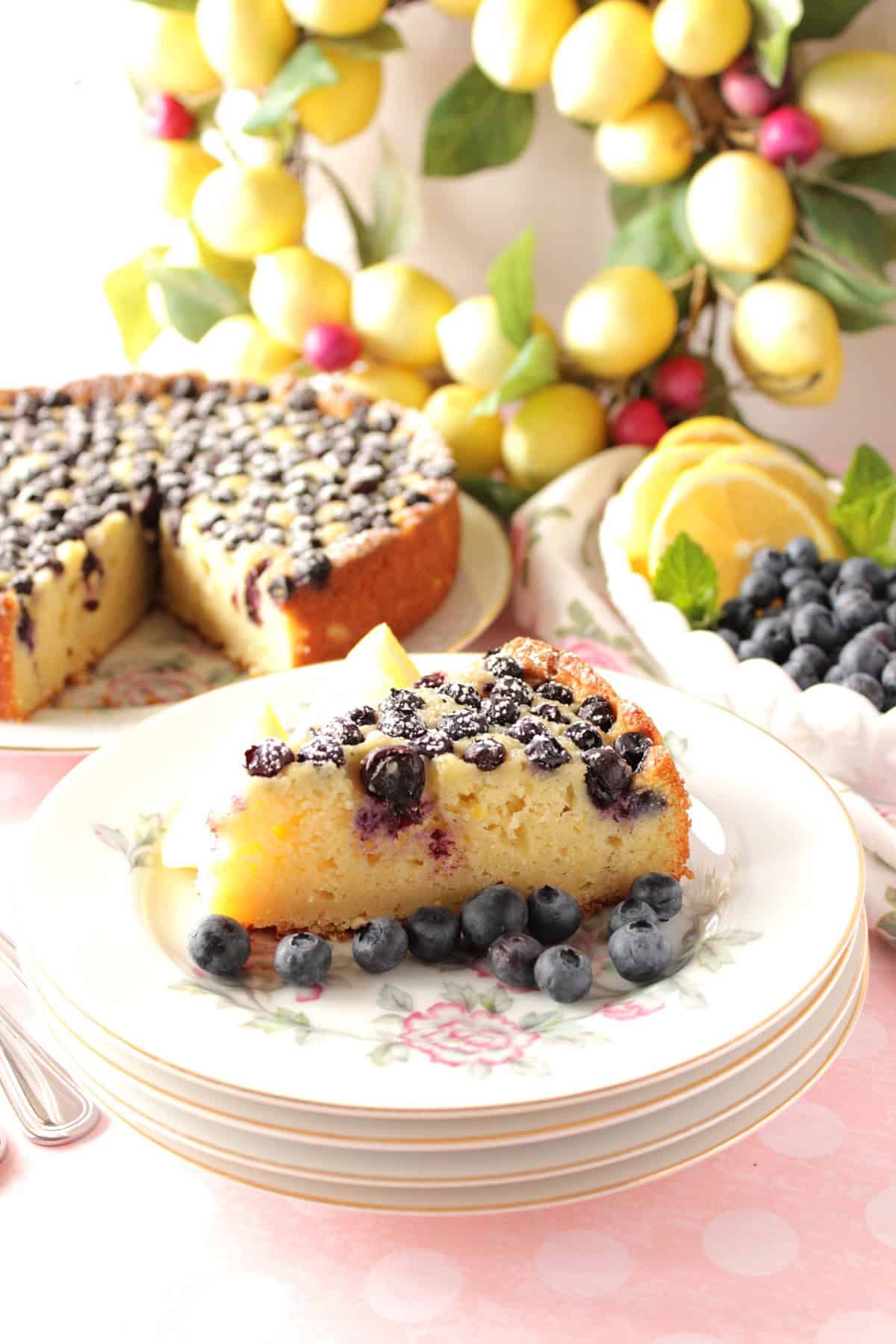 A slice of lemon ricotta cake on a stack of plates with the cake in the background.