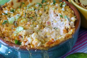 A closeup of cheesy hot Mexican Street Corn Dip with scallions and corn in a blue crock.