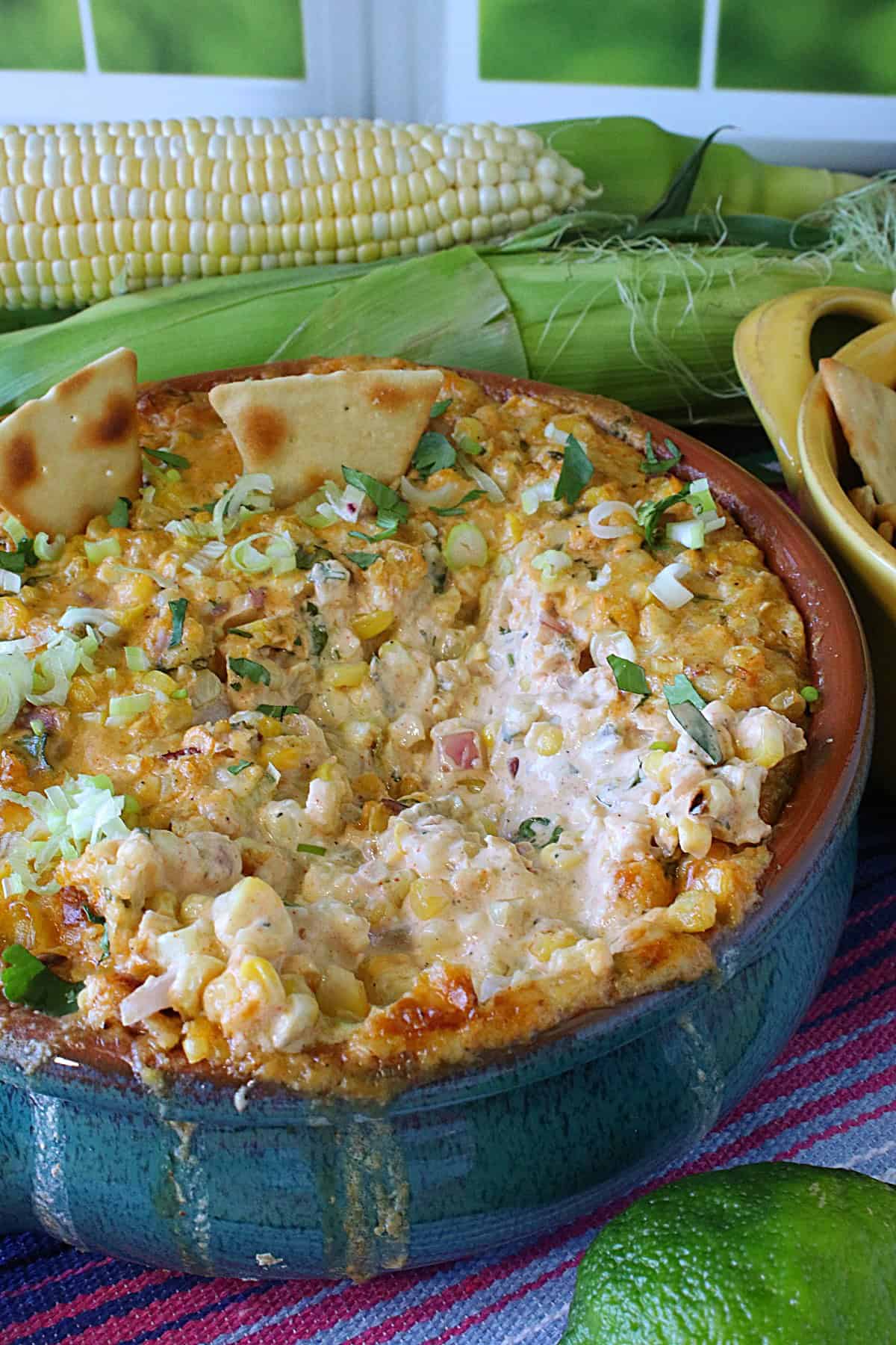 A blue crock holding hot cheesy Mexican Street Corn Dip with scallions on top.