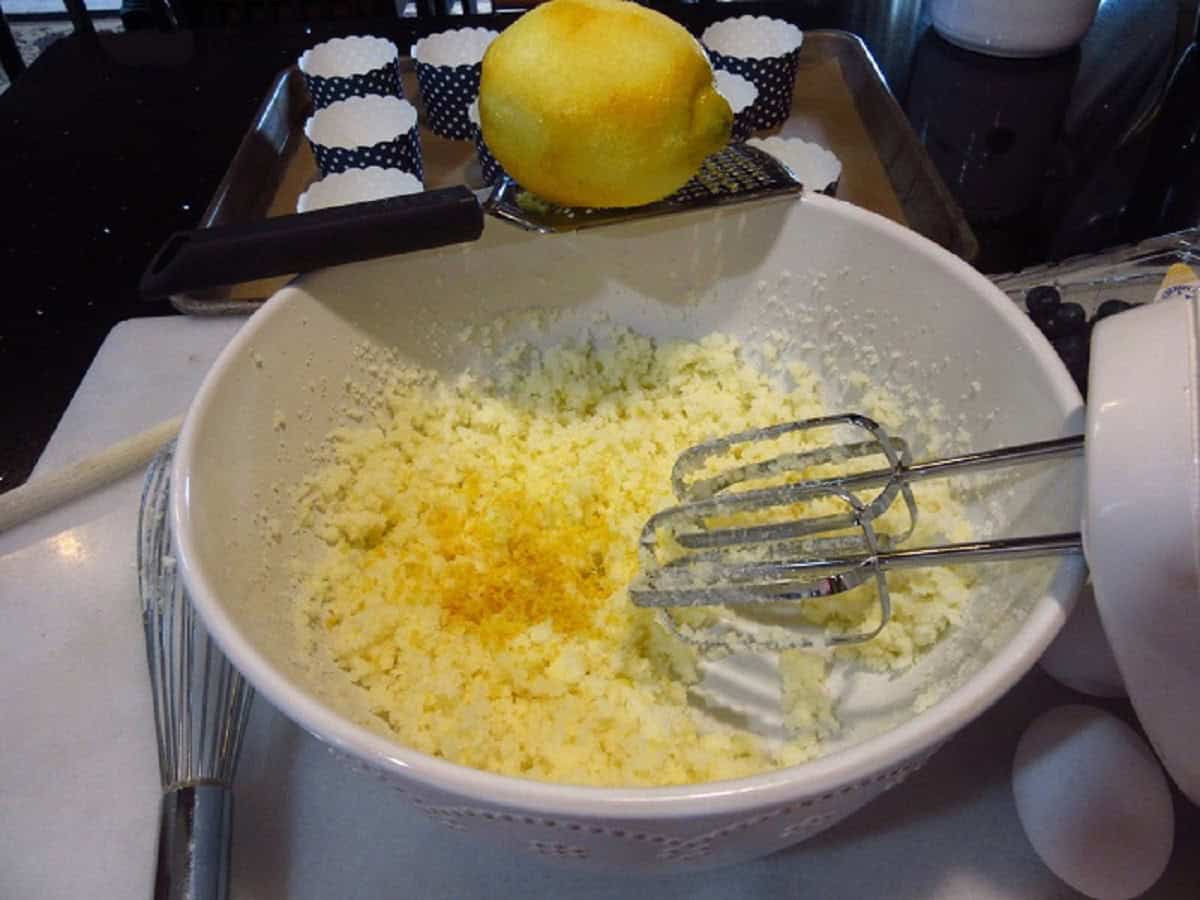 A lemon and a microplane over a bowl of batter to make blueberry muffins.
