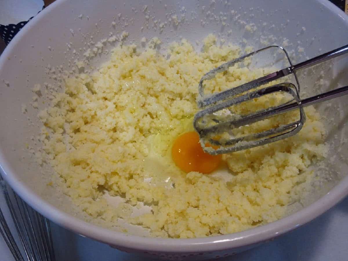 One egg in a bowl with the starting of blueberry muffin batter.