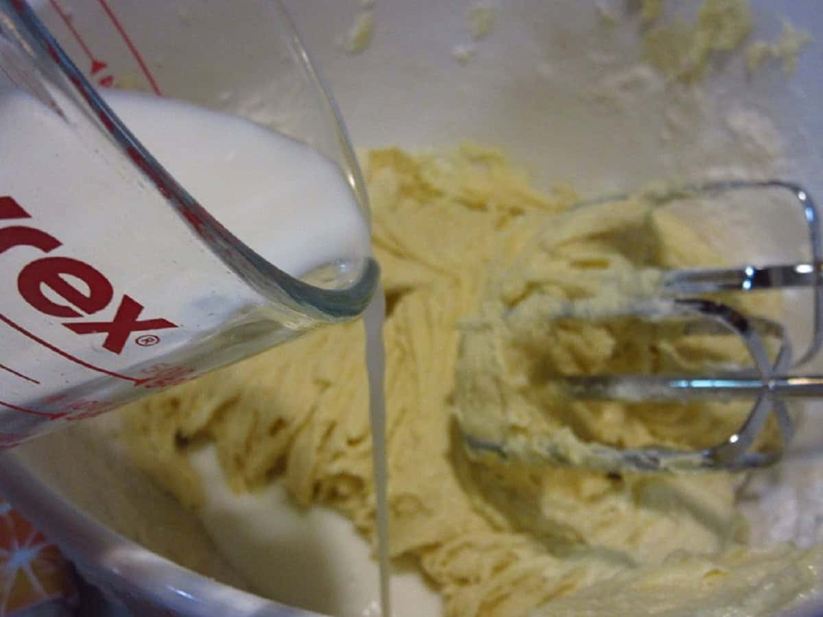 Milk being poured into a bowl with blueberry muffin batter.
