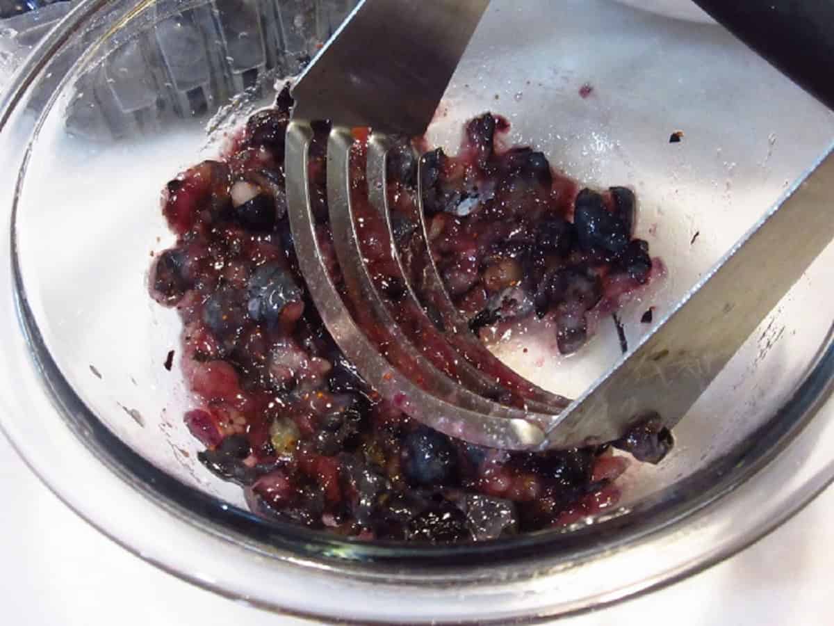 Smashing blueberries in a glass bowl with a pastry blender.