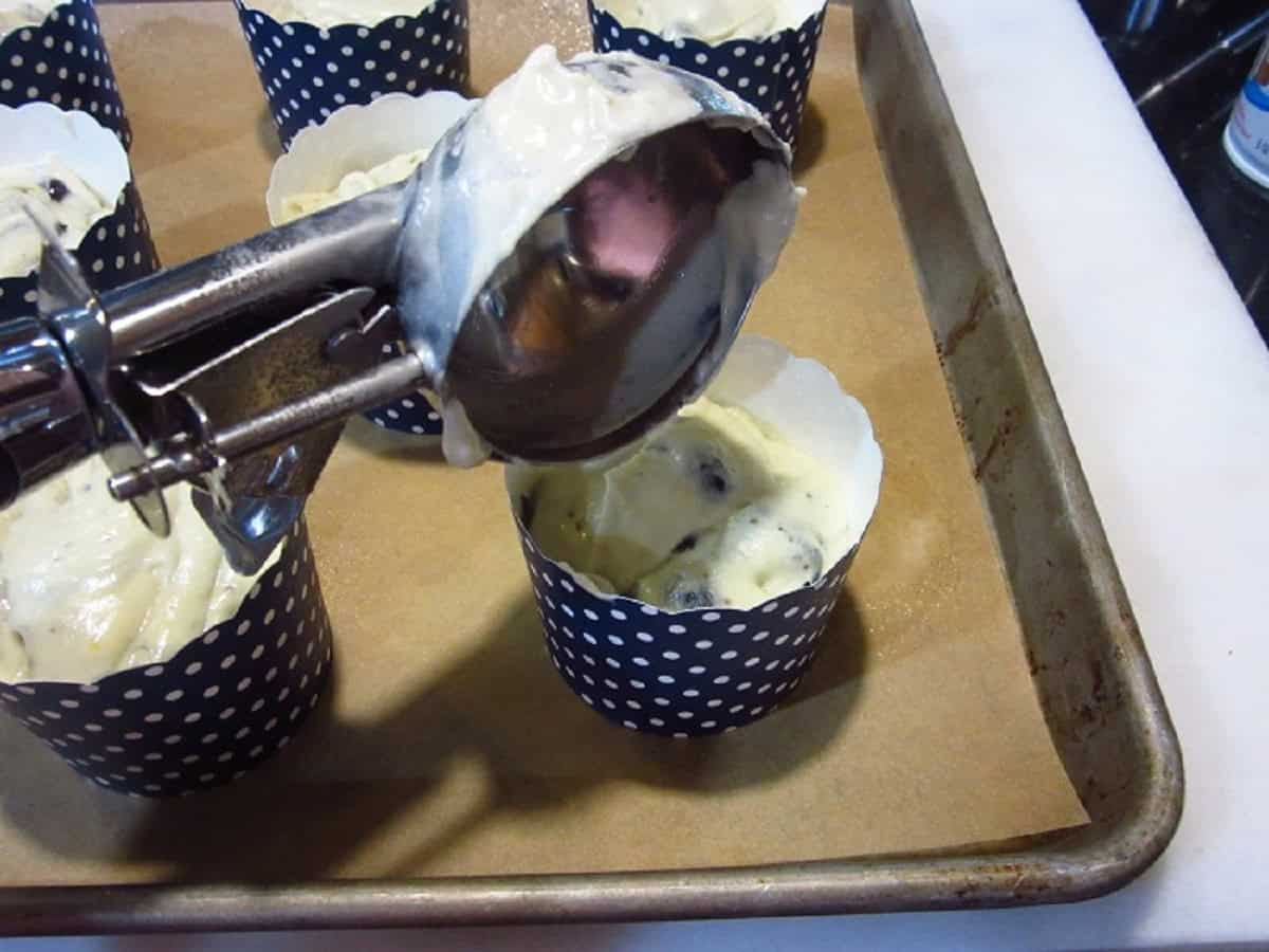 An ice cream scoop filling muffin cups with batter.