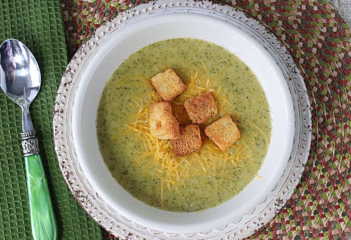 A bowl of roasted broccoli cheddar soup with a green napkin and spoon on the side.