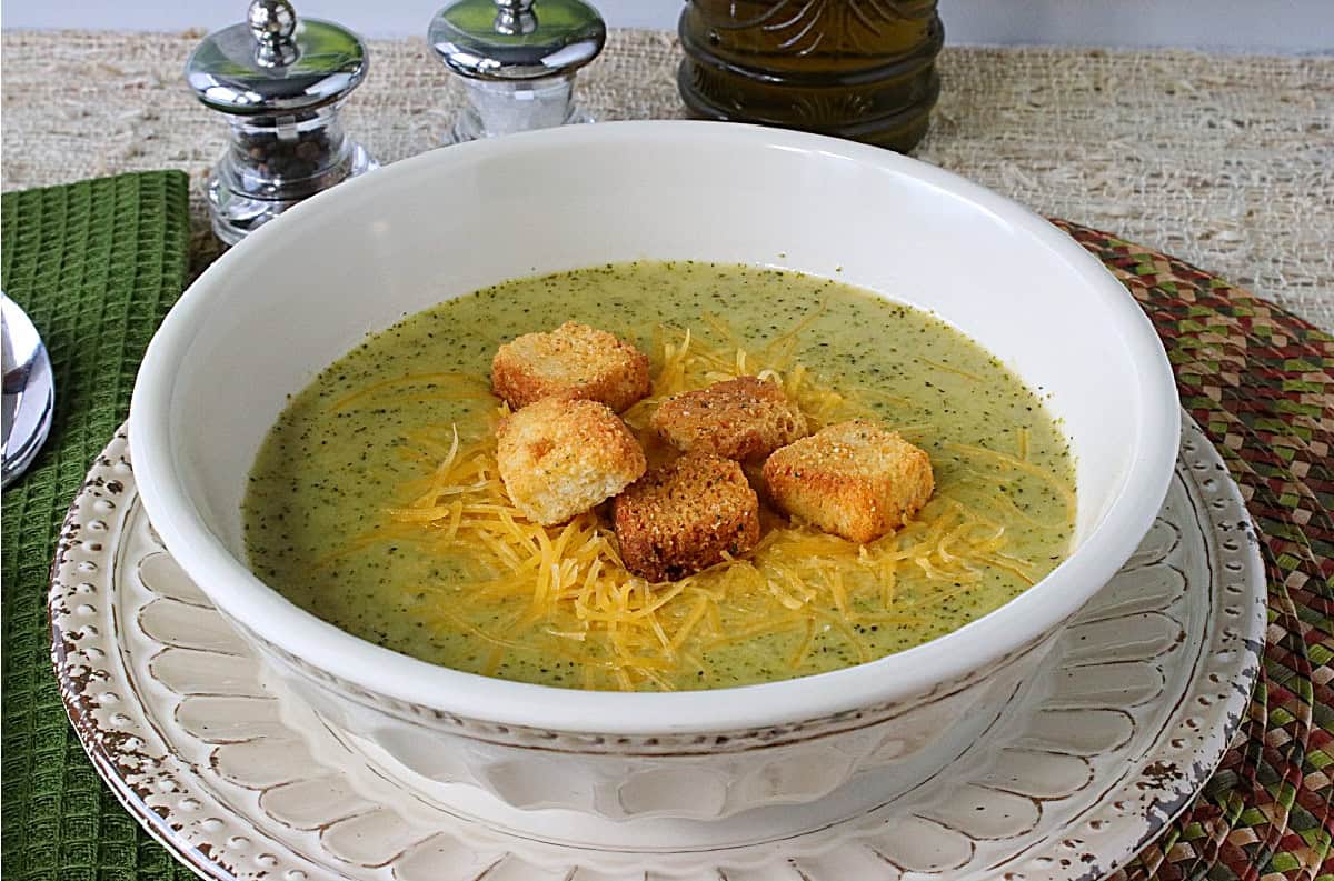 A salt and pepper shaker in the background with a bowl of broccoli cheddar soup in the foreground.