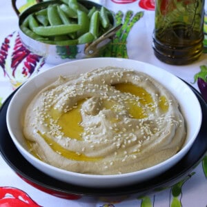 A bowl of Eggplant and Chickpea Hummus on a colorful tablecloth.