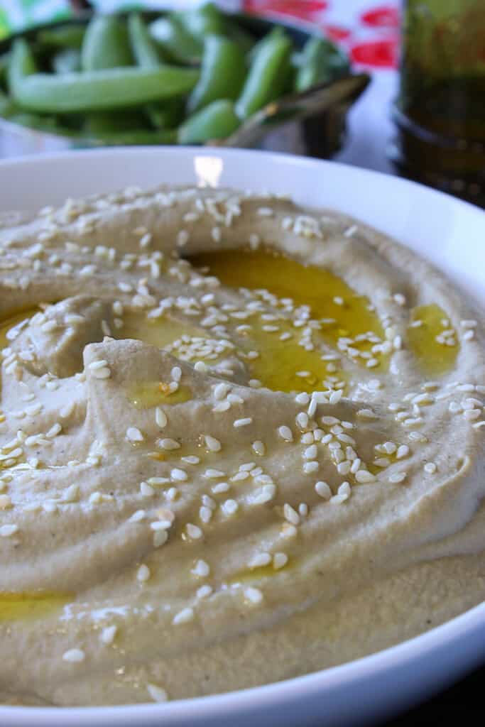 A drizzle of olive oil and sprinkling of sesame seeds on a bowl of Roasted Eggplant and Chickpea Hummus.